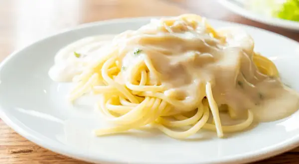 Kremowy sos serowy na makaronie spaghetti na białym talerzu.
