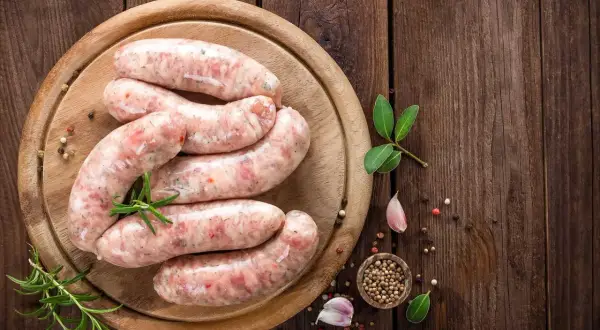 Surowa biała kiełbasa na desce, z ziołami i przyprawami. Zastanawiasz się, jak długo parzyć kiełbasę białą?