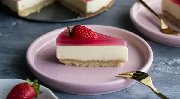 Kawałek sernika z mascarpone i galaretką truskawkową na różowym talerzyku.