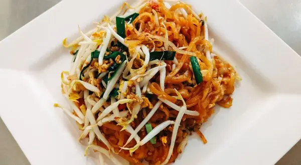 Pad thai z kiełkami fasoli mung, szczypiorkiem i orzeszkami ziemnymi na białym talerzu.