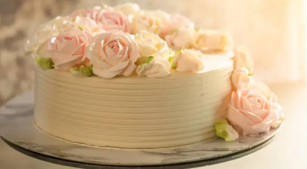 Tort udekorowany kremowymi różami w pastelowych kolorach.