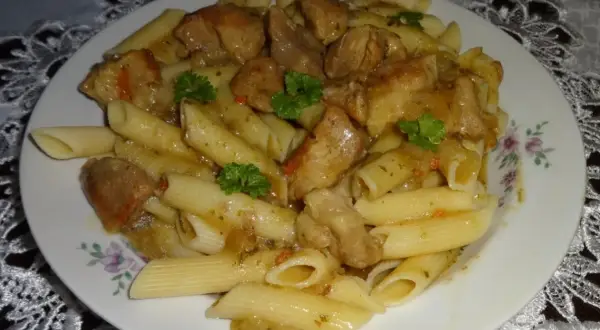 Penne z soczystym makaronem z mięsem wieprzowym w sosie, udekorowane natką pietruszki.