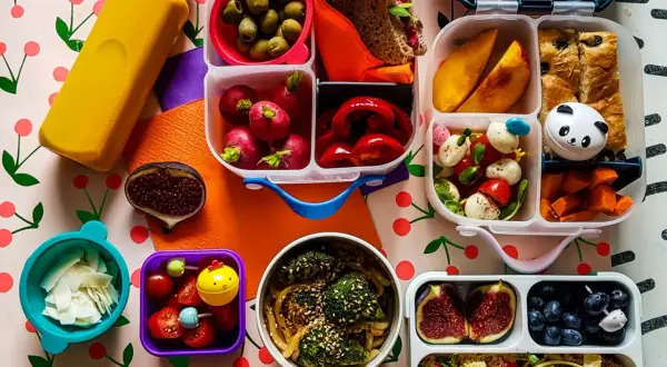 Kolorowy lunchbox z owocami, warzywami, kanapką i napojem.
