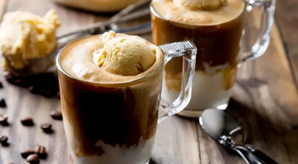 Dwa kubki affogato z lodami waniliowymi i kawą, na drewnianym stole z ziarnami kawy.
