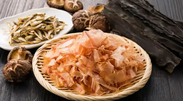 Suszone rybki, grzyby shiitake, płatki bonito i wodorosty kombu na drewnianym tle.