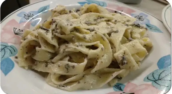 Pappardelle z kremowym sosem, w którym wyczuwalne są kawałki trufli. Makaron z pastą truflową i śmietaną wygląda apetycznie.