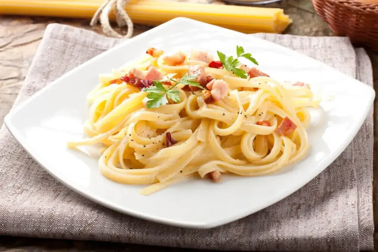 Talerz spaghetti carbonara z boczkiem i natką pietruszki.
