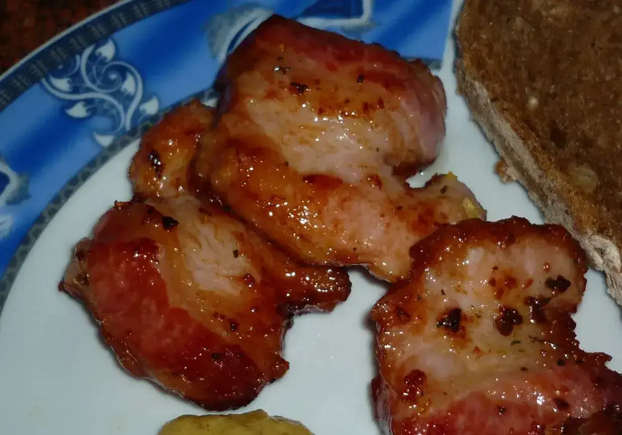 Usmażony boczek z przyprawami na talerzu, obok kromka chleba.