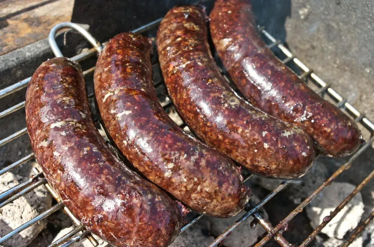 Cztery soczyste kaszanki z grilla pieką się na ruszcie, uwalniając apetyczny aromat.