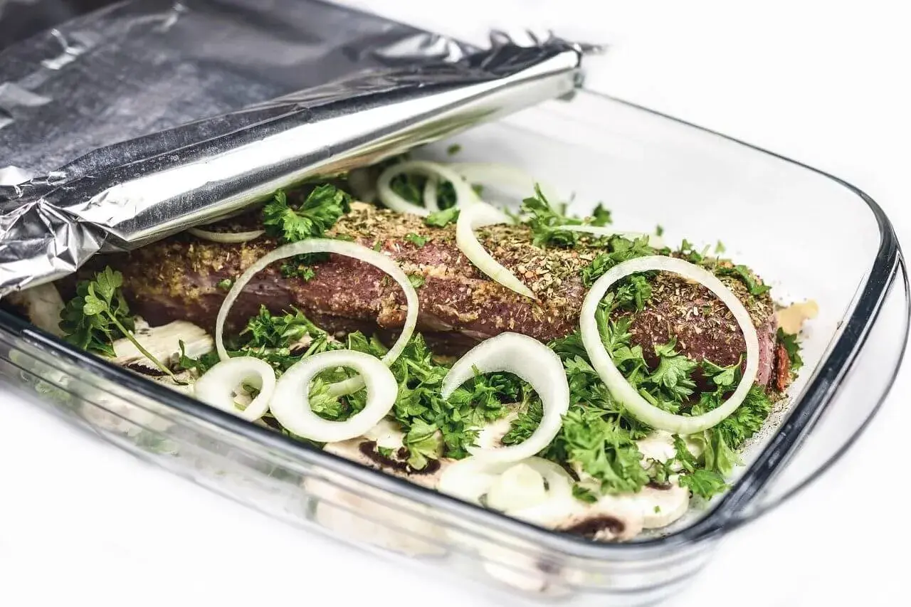 Mięso w naczyniu żaroodpornym pod folią aluminiową, z cebulą i ziołami.