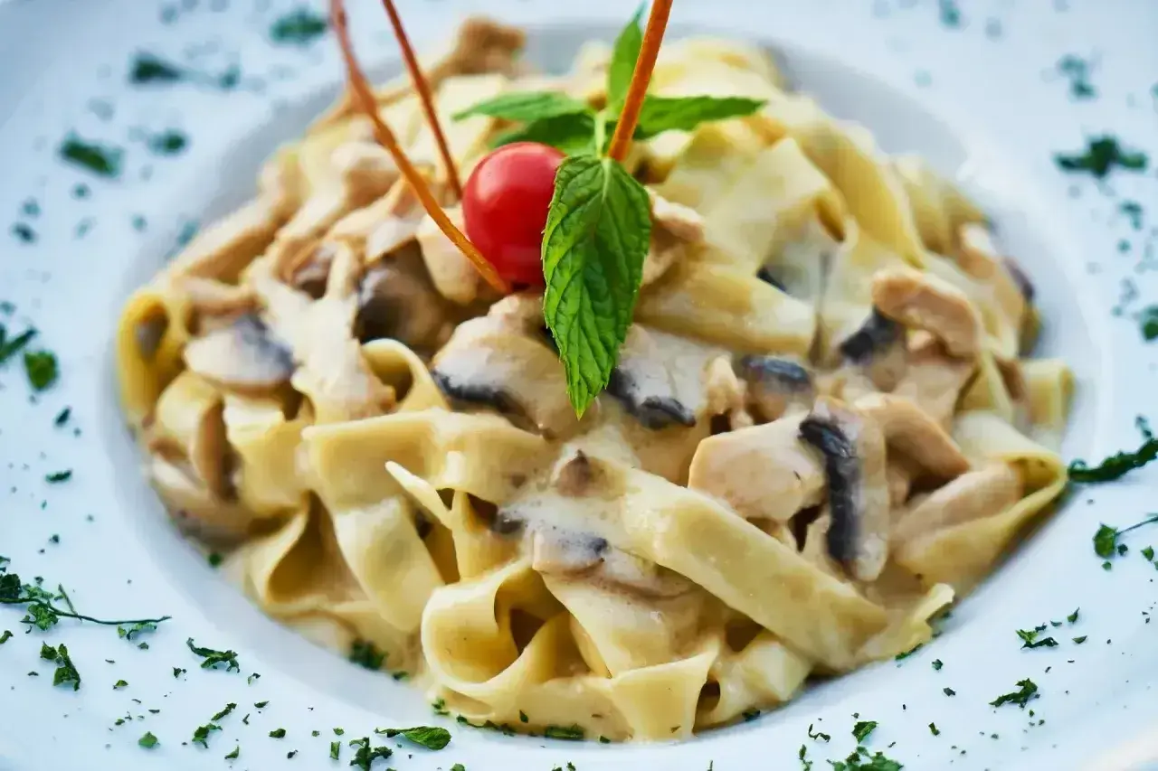 Tagliatelle z kurczakiem i grzybami w sosie śmietanowym, udekorowane pomidorkiem i miętą.