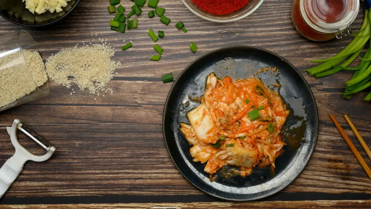 Talerz z kimchi, obok składniki: sezam, czosnek, papryka, szczypiorek, obieraczka i pałeczki.