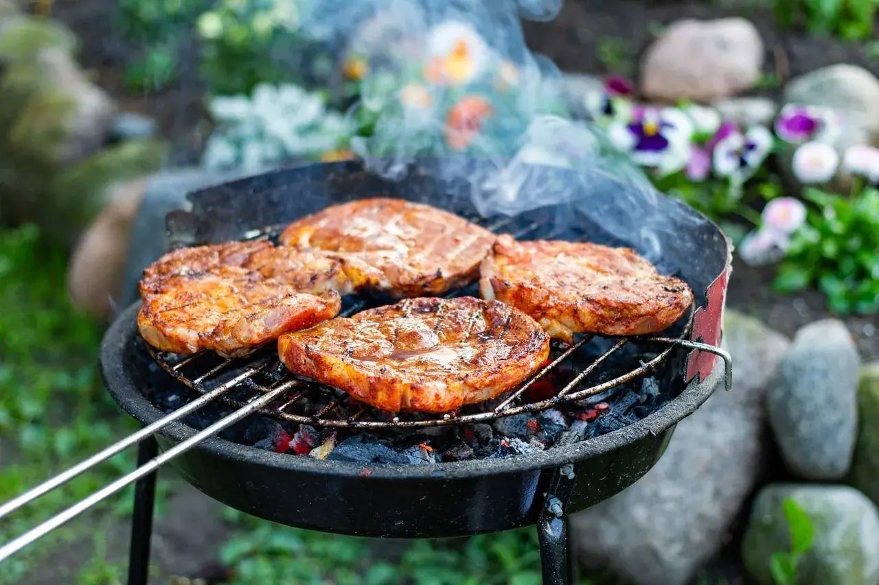 Soczysty karczek na grillu, idealny przykład, jak zamarynować karczek na grilla. Dym unosi się nad grillowanymi mięsami.