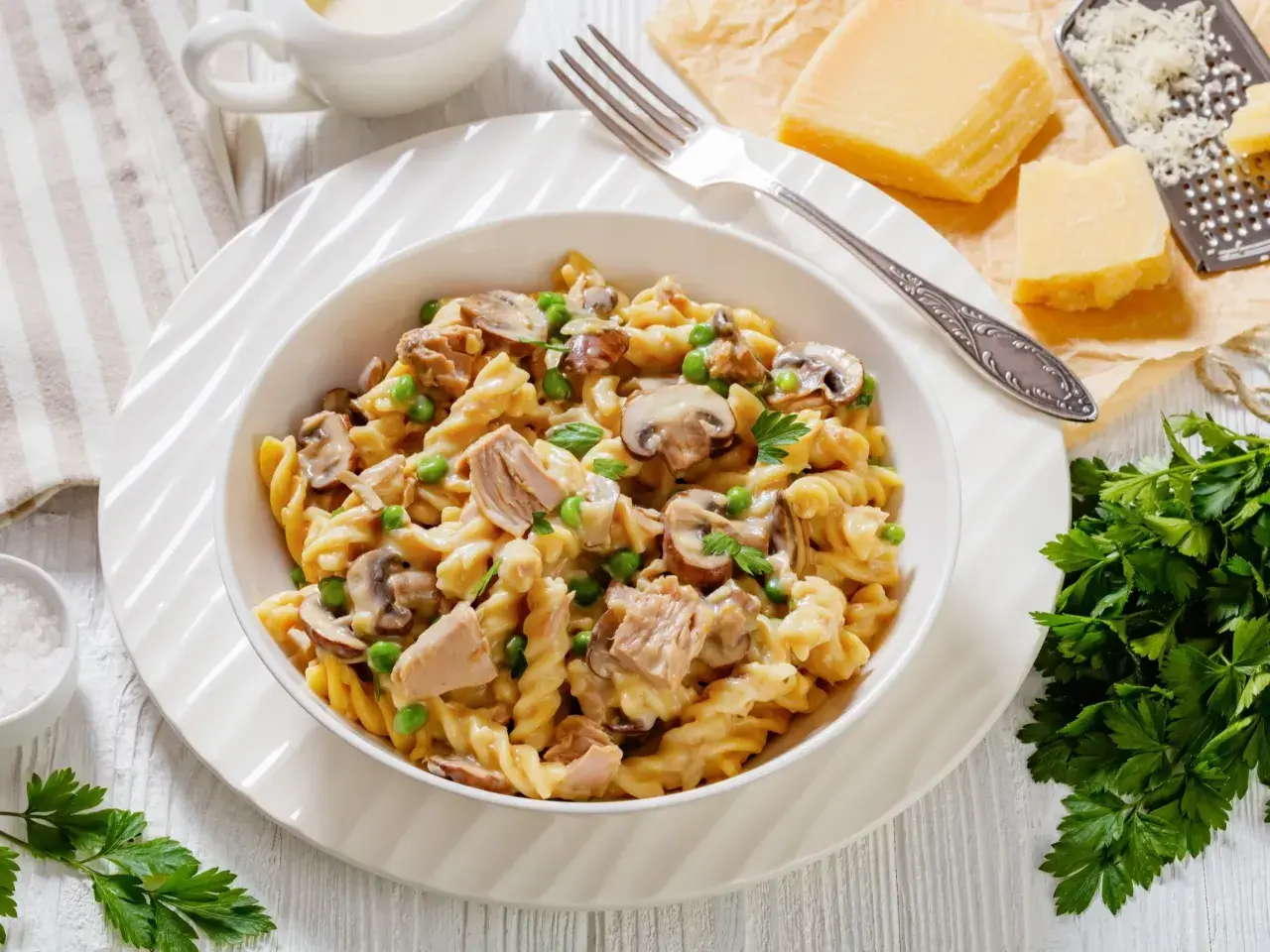 Makaron fusilli z tuńczykiem, groszkiem i pieczarkami w kremowym sosie, udekorowany natką pietruszki.