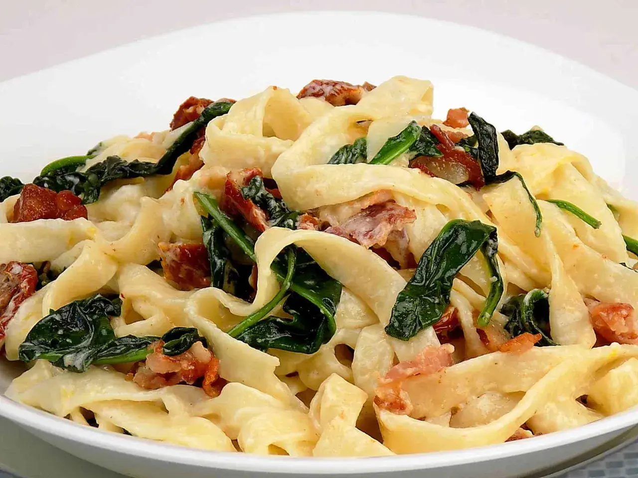 Makaron tagliatelle z kremowym sosem, szpinakiem i kawałkami boczku.