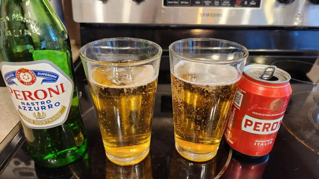 Butelka i puszka Peroni Nastro Azzurro obok dwóch szklanek piwa.
