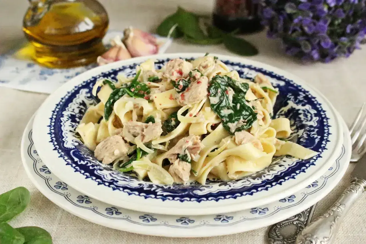 Makaron tagliatelle z tuńczykiem i szpinakiem w kremowym sosie, podany na talerzu z niebieskim wzorem.