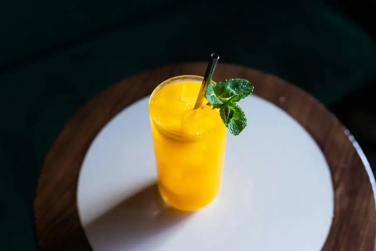 Jasny, żółty koktajl mango w szklance z miętą i metalową słomką na drewnianym blacie.