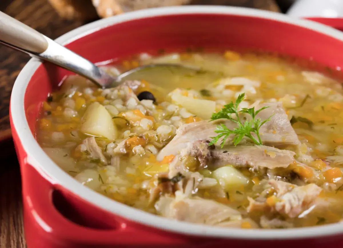 Miseczka domowego krupniku z mięsem, ziemniakami i kaszą jęczmienną, ozdobiona natką pietruszki.