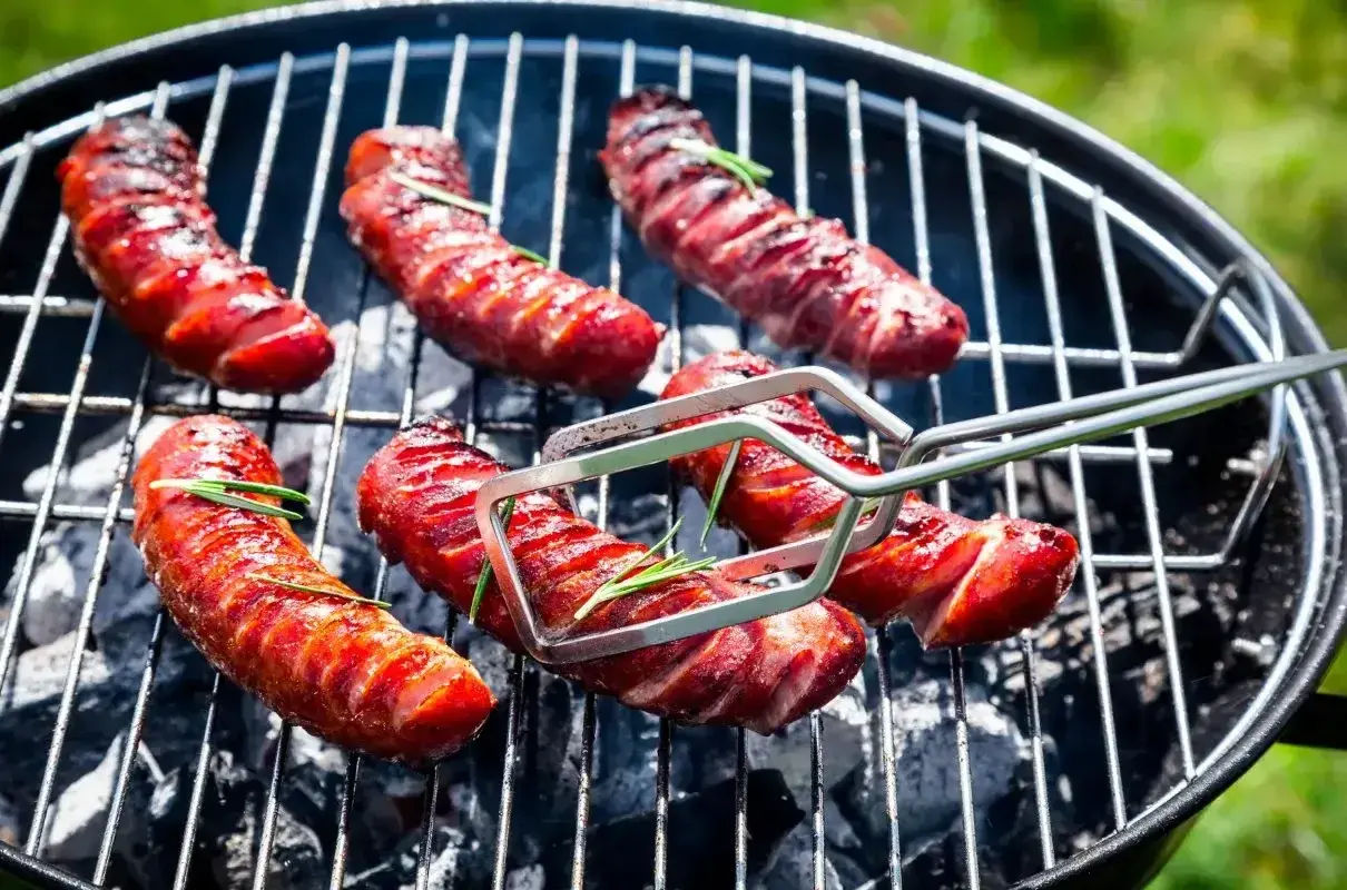 Kiełbaski grillowane na ruszcie, z gałązkami rozmarynu, w zbliżeniu.