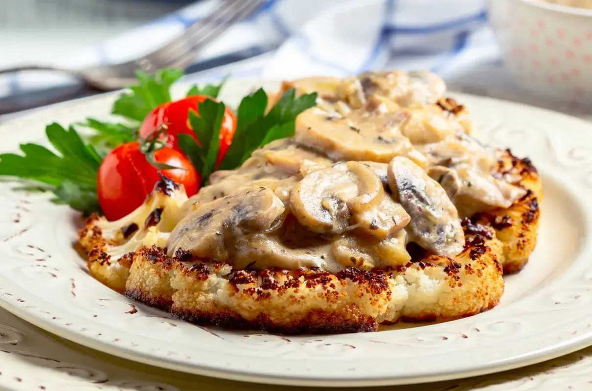 Grillowany kalafior w sosie grzybowym z pomidorkami i natką pietruszki na talerzu.