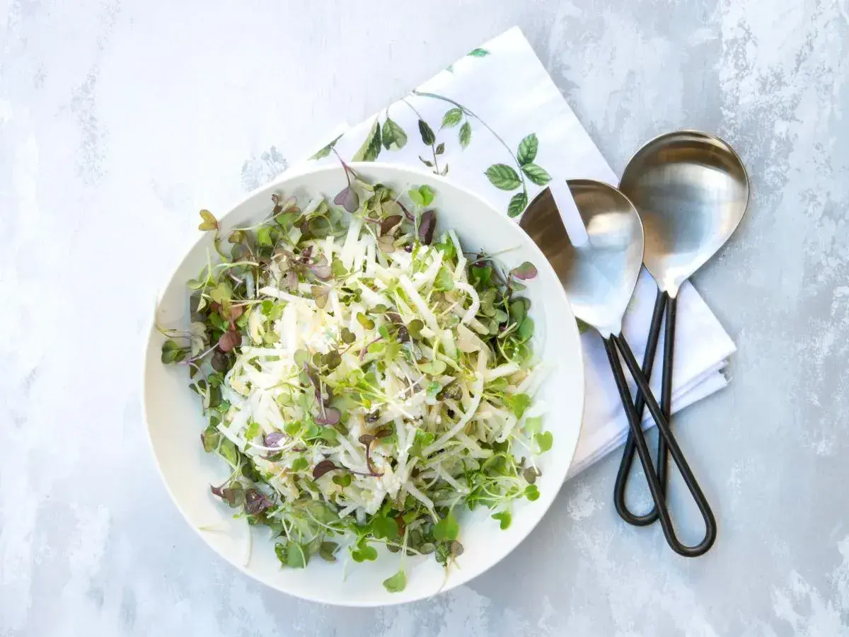 Sałatka coleslaw z kiełkami w białej misce, obok serwetka i łyżki do sałatek.