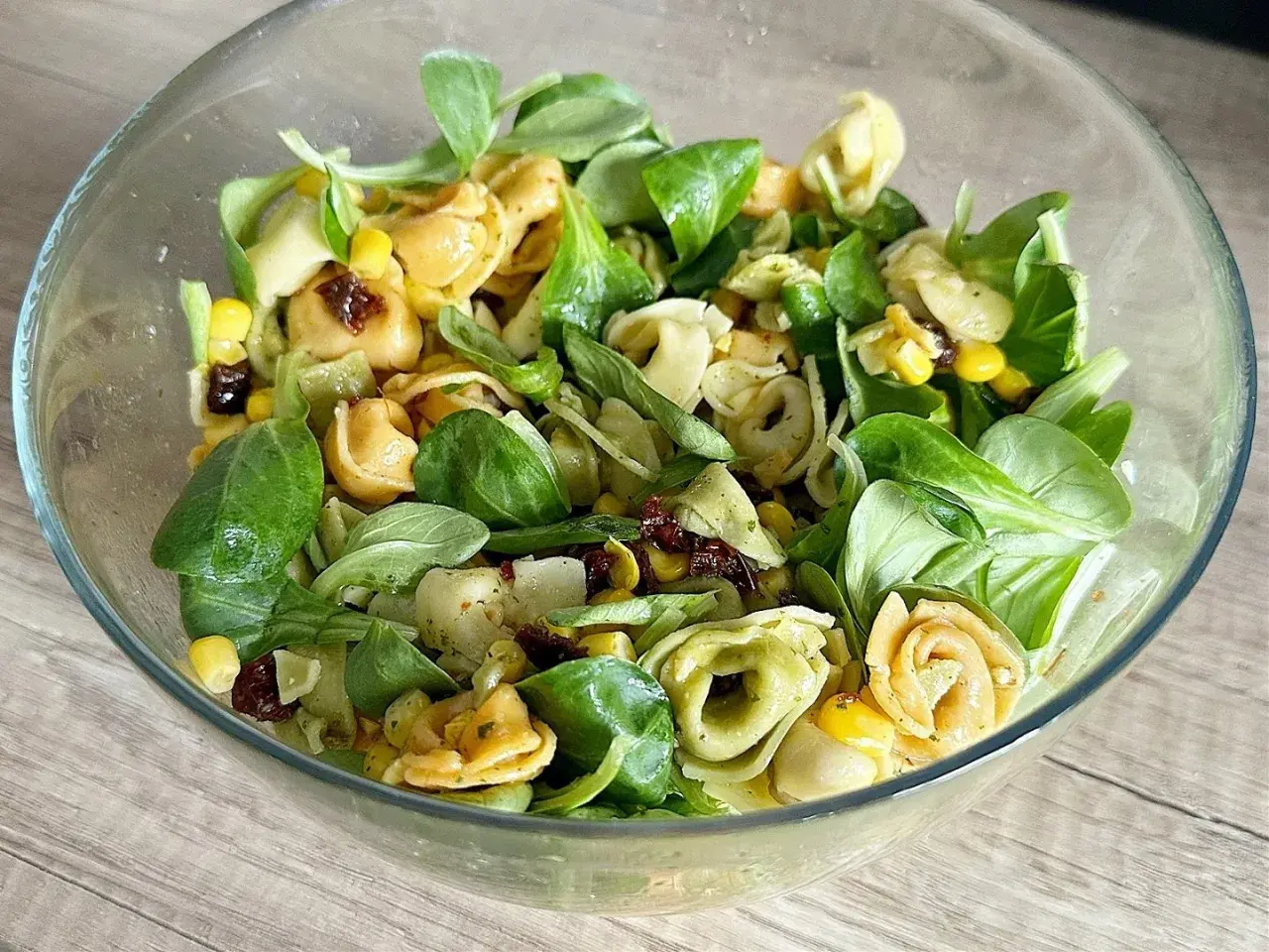Sałatka z tortellini, kukurydzą, suszonymi pomidorami i zieloną sałatą w szklanej misce.