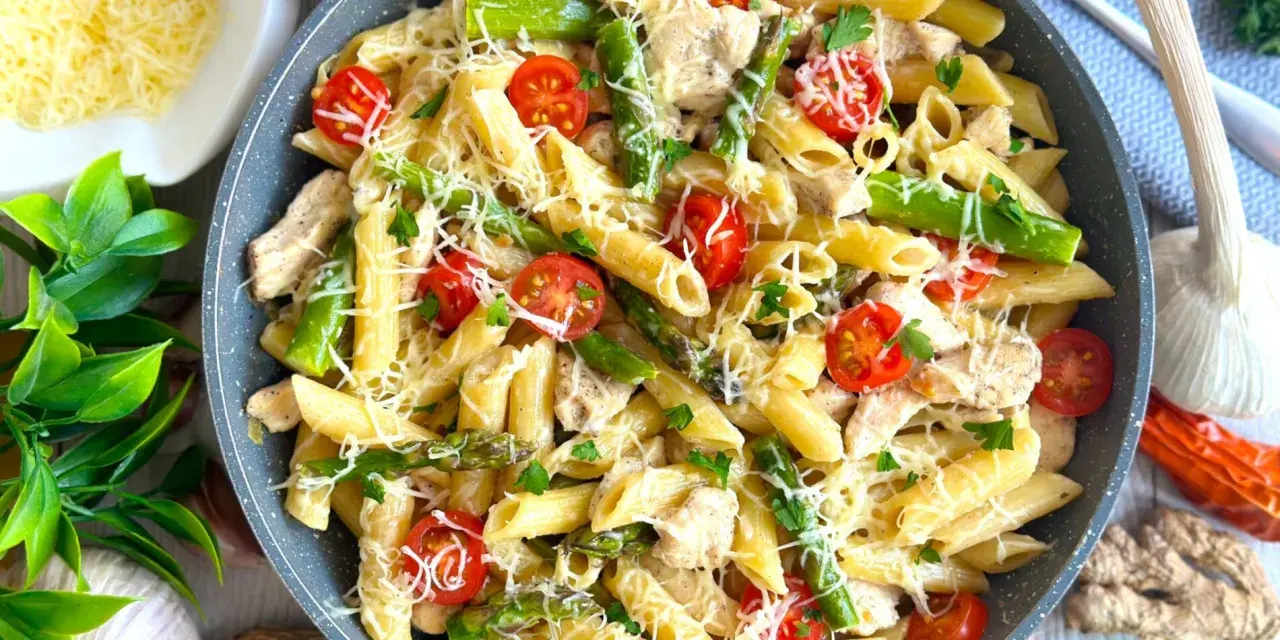 Makaron penne z kurczakiem, szparagami i pomidorkami koktajlowymi, posypany serem.