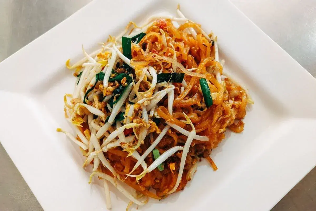 Pad thai z kiełkami fasoli mung, szczypiorkiem i orzeszkami ziemnymi na białym talerzu.