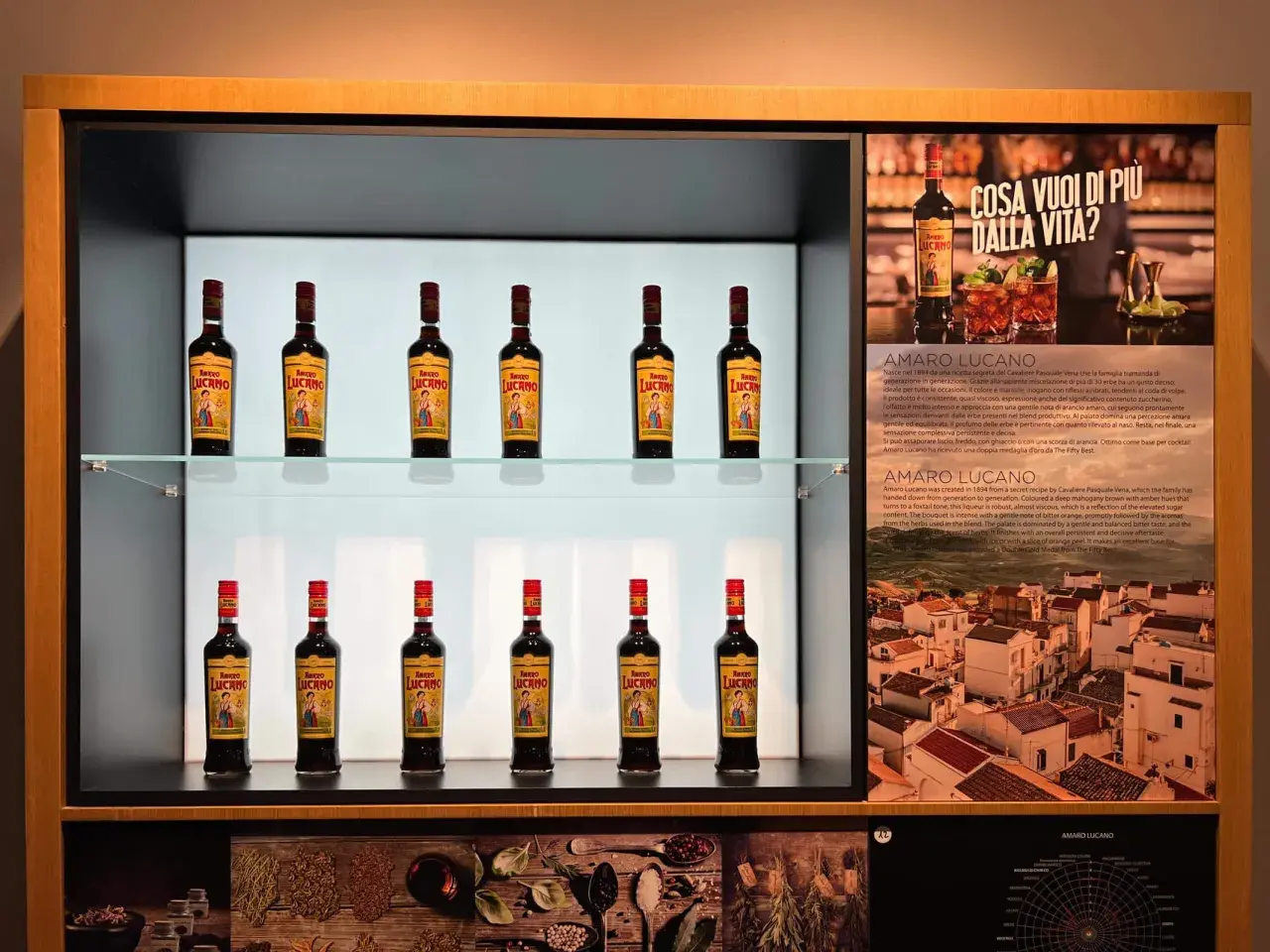 Butelki likieru Amaro Lucano ustawione na półkach, obok opisu produktu i włoskiego krajobrazu.