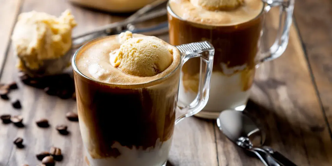 Dwa kubki affogato z lodami waniliowymi i kawą, na drewnianym stole z ziarnami kawy.