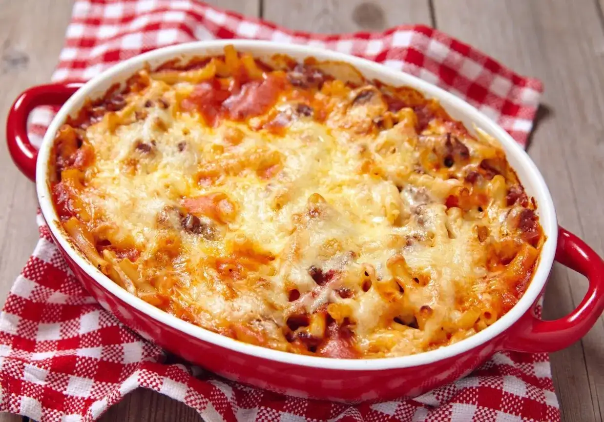 Zapiekanka makaronowa z mięsem mielonym i roztopionym serem w czerwonym naczyniu.
