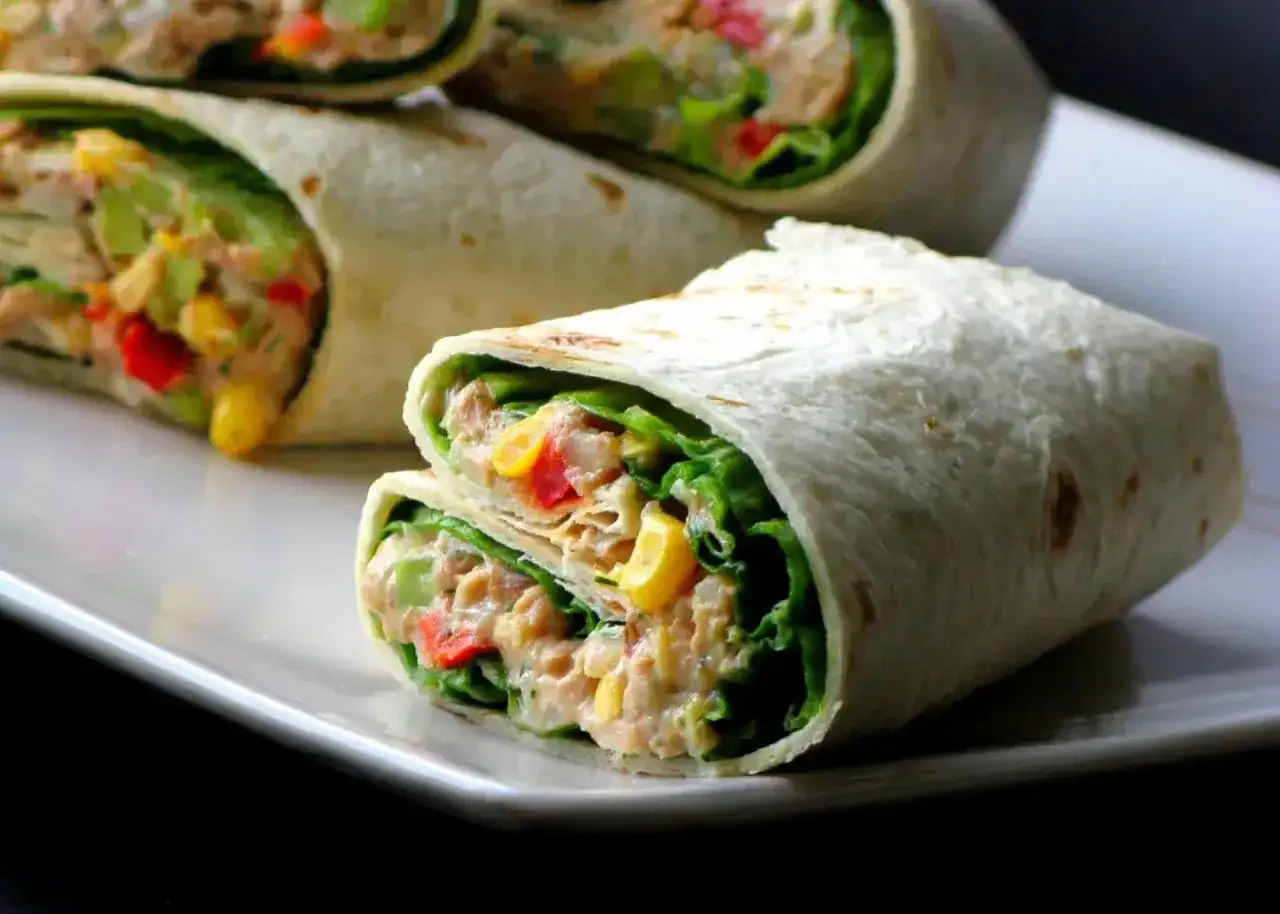 Tortilla z tuńczykiem, kukurydzą, papryką i sałatą na białym talerzu.