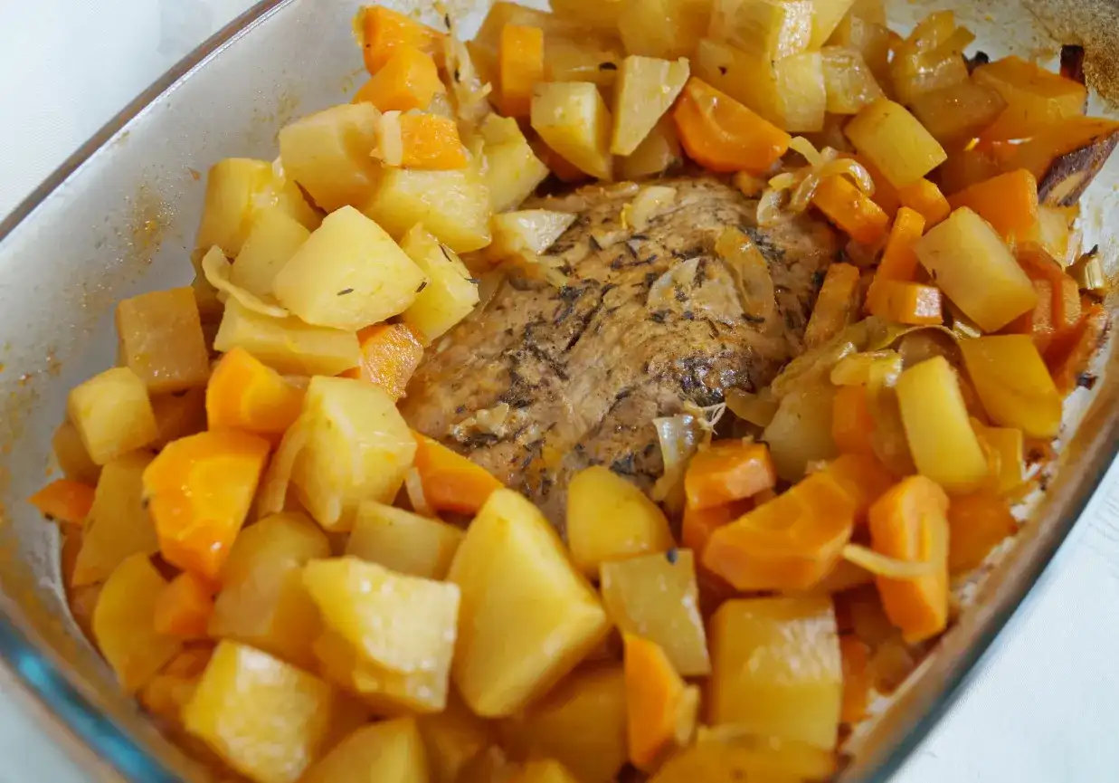 Pyszne mięso pieczone w piekarniku z ziemniakami i marchewką, aromatyczne zioła podkreślają smak dania.