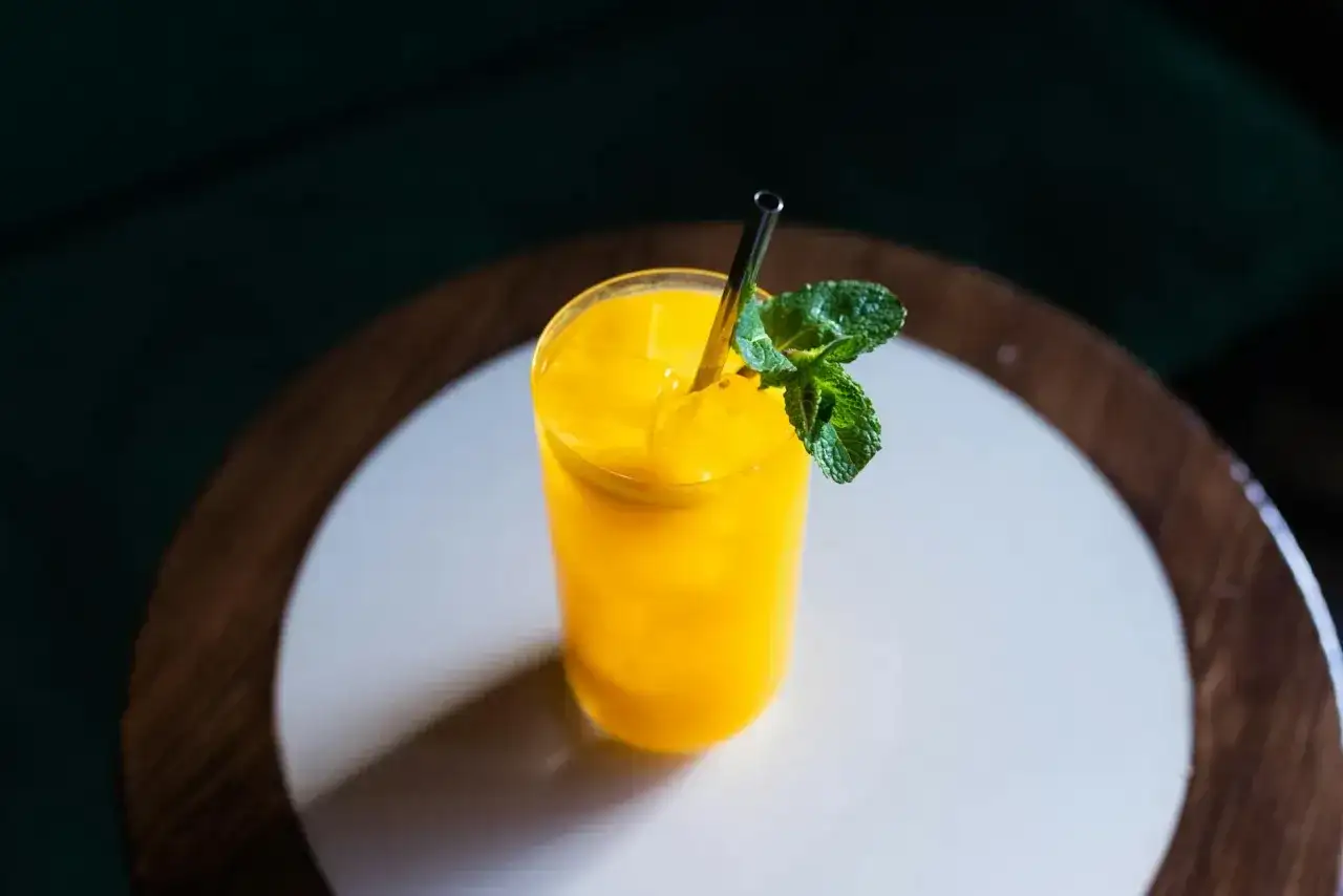 Jasny, żółty koktajl mango w szklance z miętą i metalową słomką na drewnianym blacie.