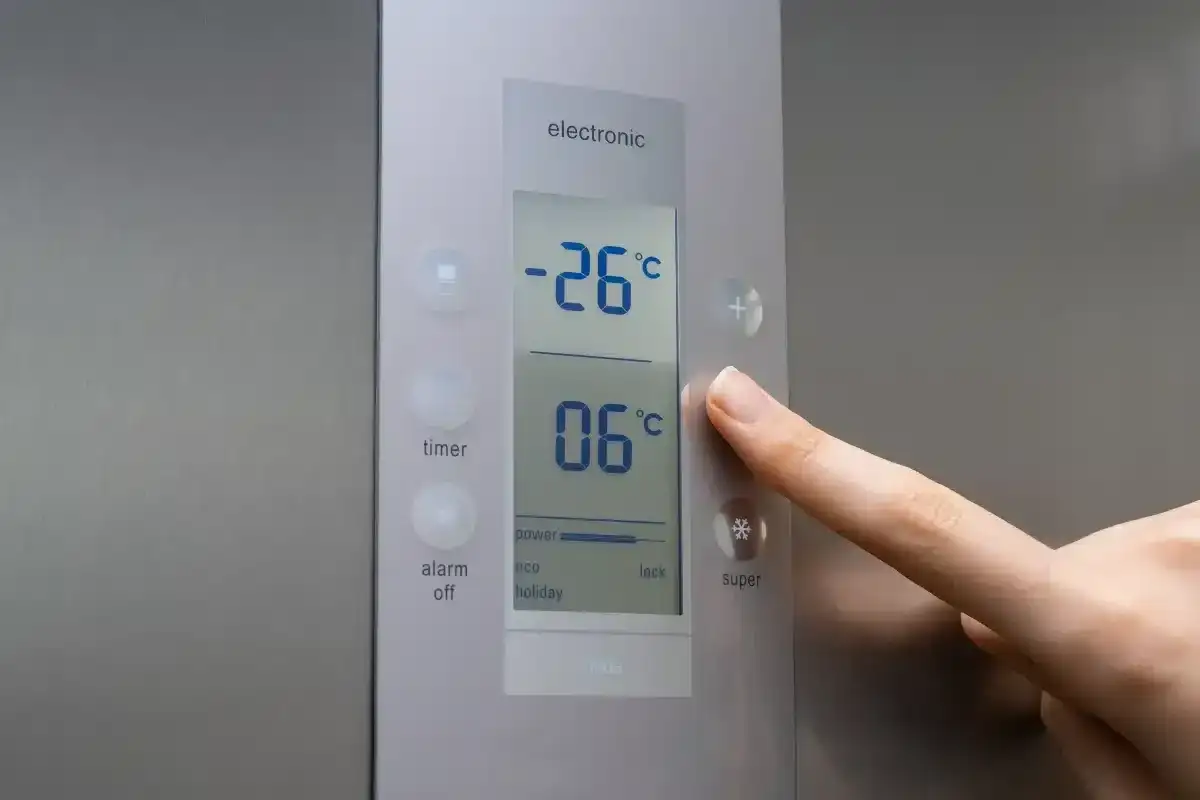 Dłoń naciska przycisk na panelu sterowania lodówki z wyświetlaczem temperatury.
