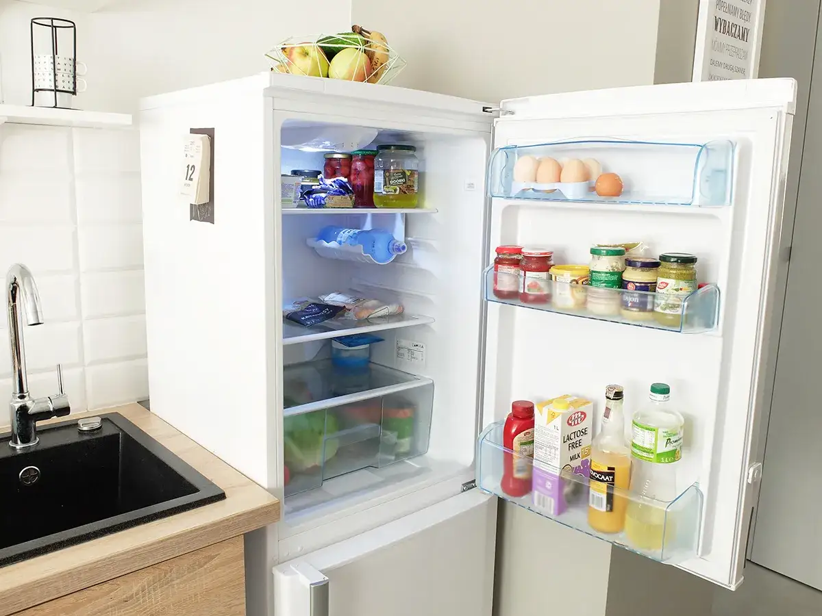 Otwarta lodówka pełna produktów: słoiki, jajka, mleko, napoje. Zastanawiasz się, ile można trzymać zupę w lodówce? Tu znajdziesz inspiracje.