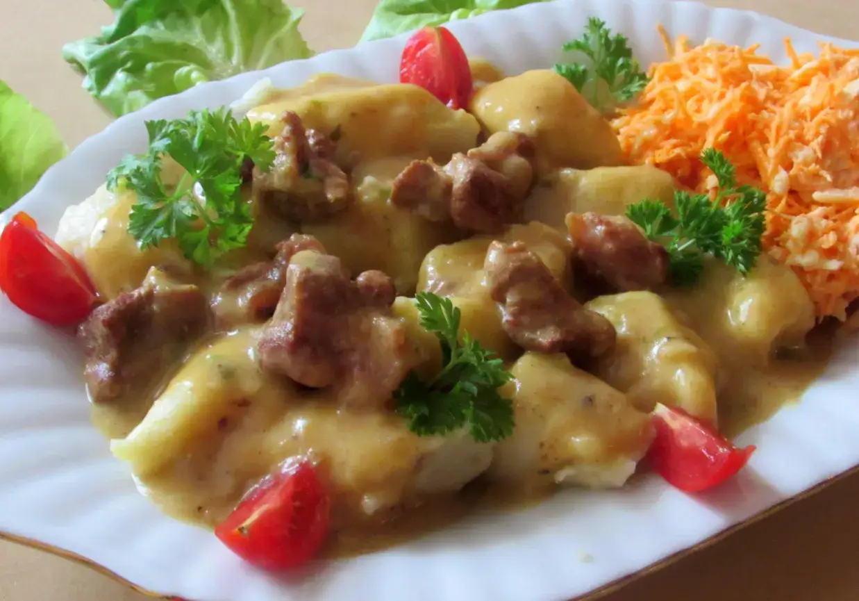 Kopytka w sosie z mięsem, udekorowane pomidorkami i natką pietruszki. Idealne danie, które pasuje do kopytek.