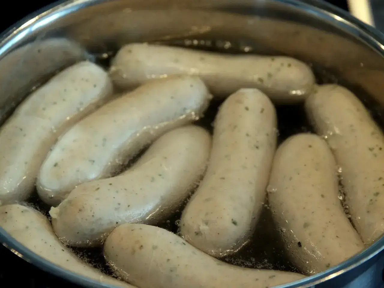 Biała kiełbasa gotuje się w garnku. Kluczowe jest utrzymanie odpowiedniej temperatury, by nie pękła.