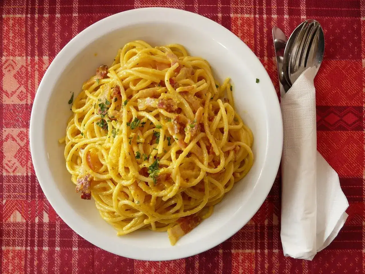 Porcja spaghetti carbonara na talerzu, z boczkiem i pietruszką. Zastanawiasz się, ile kalorii ma makaron spaghetti w takim wydaniu?