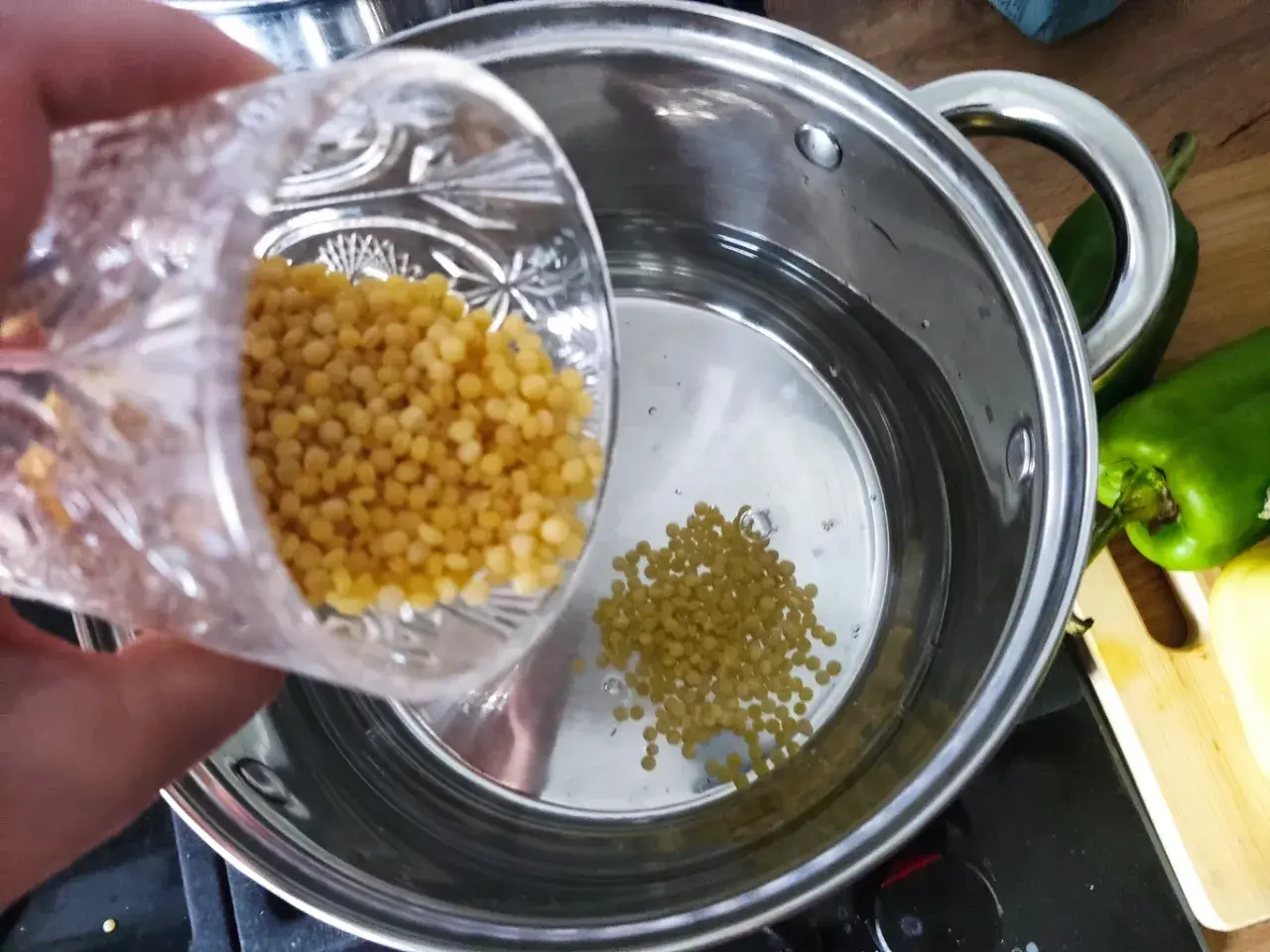 Wsypywanie kuskusu perłowego do gotującej się wody w garnku.