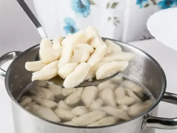 Kopytka gotujące się w garnku, wyjmowane łyżką cedzakową.