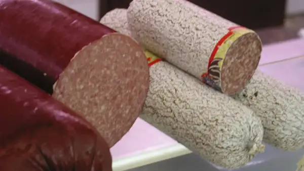 Kawałki ciemnej i jasnej kiełbasy salami, jedna przekrojona.