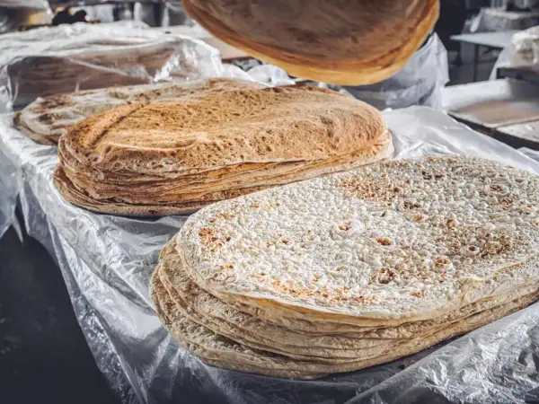 Stos cienkich, okrągłych placków lawaszu na stole, niektóre z nich lekko przypieczone.