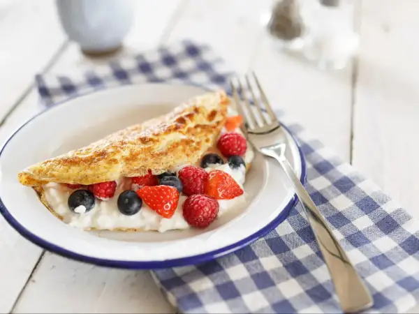 Puszysty omlet z serkiem i owocami leśnymi na talerzu.