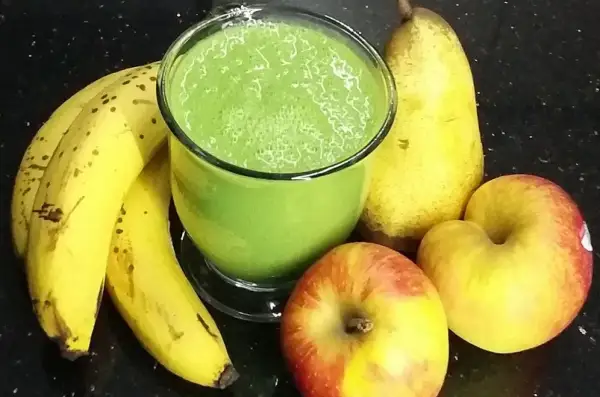 Zielony koktajl w szklance otoczony bananami, jabłkami i gruszką.