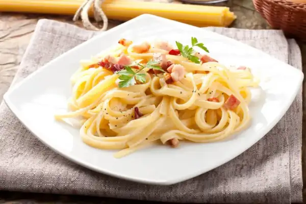 Talerz spaghetti carbonara z boczkiem i natką pietruszki.