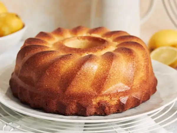 Puszysta babka z wgłębieniem pośrodku, na talerzu, z cytrynami w tle.