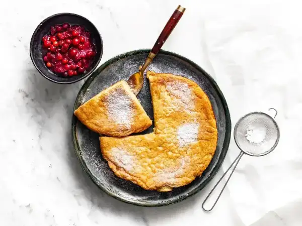 Puszysty omlet posypany cukrem pudrem, podany z żurawiną i łyżką.