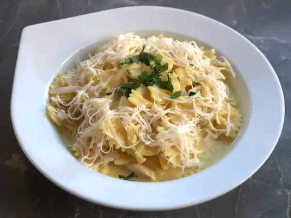 Szybki obiad z twarogiem: makaron farfalle w kremowym sosie, posypany startym serem i natką pietruszki.